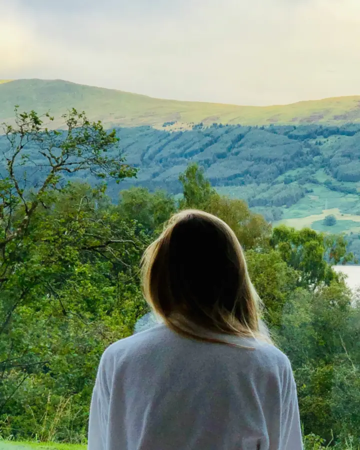 Woman in a bathrobe, seen from behind, looking out at the hills and the lake